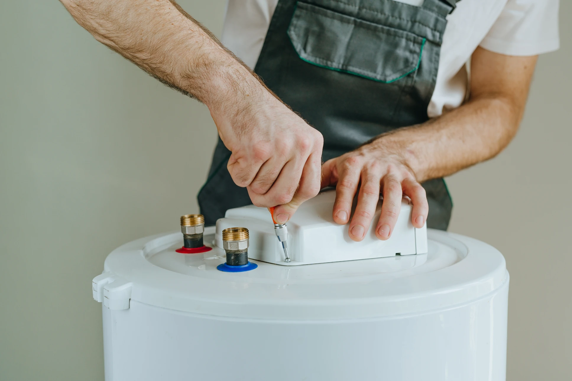 Technicien en combinaison bleue et gants de protection répare une machine à laver blanche dans une buanderie domestique